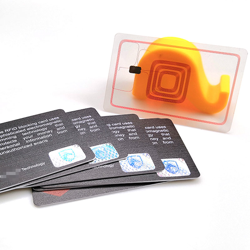 การ์ดบล็อก RFID แบบพัดถูกจัดแสดงพร้อมอินเลย์เสาอากาศและชิปที่มองเห็นได้บนฐานตั้งสีเหลืองเพื่อแสดงโครงสร้างการป้องกันภายใน