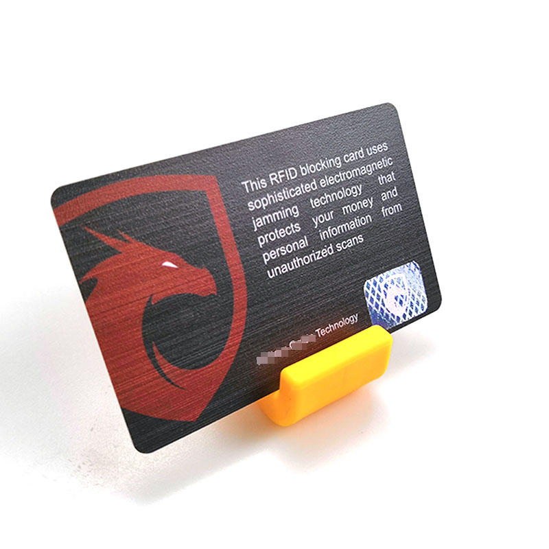 บัตรบล็อกสัญญาณ RFID ใบเดียวบนที่วางสีส้ม แสดงโลโก้โล่สีแดงและข้อความเกี่ยวกับการบล็อกการสแกน RFID ที่ไม่ได้รับอนุญาต