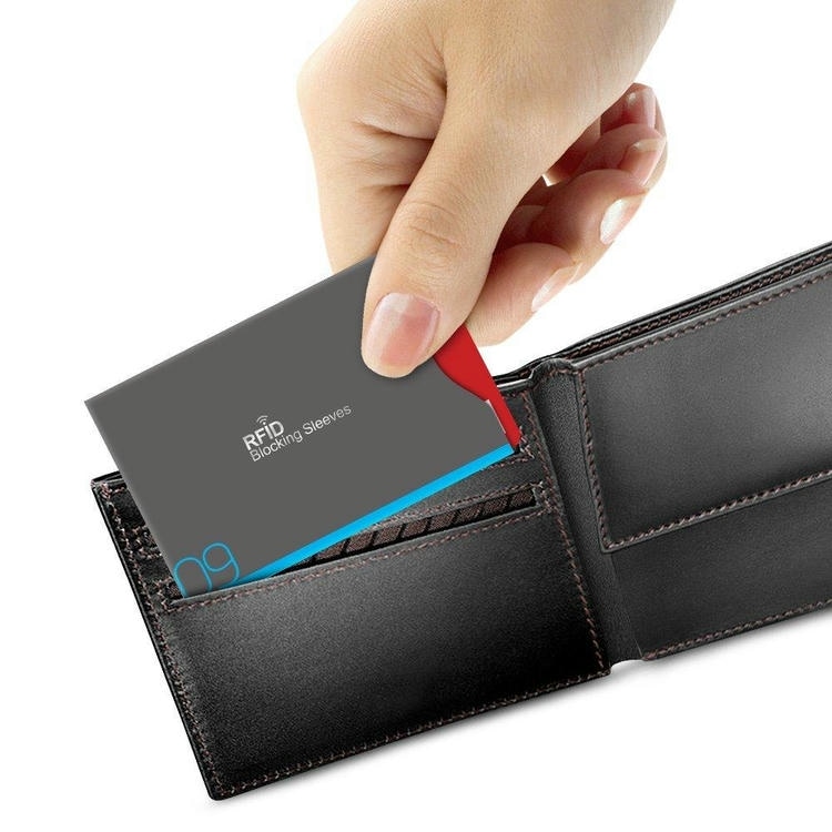 มือกำลังใส่ซอง RFID บล็อกสัญญาณลงในกระเป๋าสตางค์หนัง แสดงการใช้งานกระเป๋าสตางค์กันขโมยจริงเพื่อความเป็นส่วนตัวของบัตร