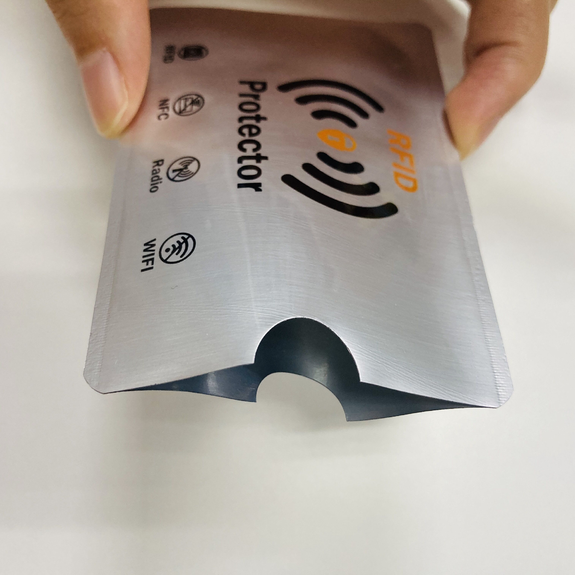 มือบีบซองกันสัญญาณ RFID ให้เปิดออกเพื่อแสดงรูปทรงปากช่องและโครงสร้างกันสัญญาณแบบหลายชั้นที่ช่องบาก