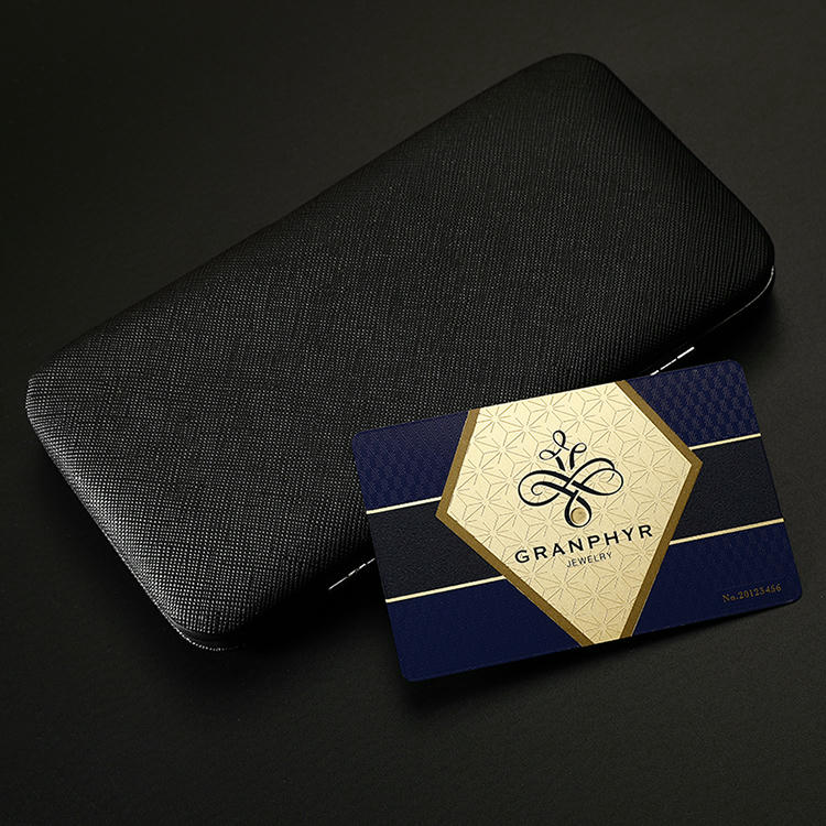 นามบัตรโลหะสีน้ำเงินและทองวางอยู่ข้างกล่องของขวัญสีดำ แสดงบรรจุภัณฑ์หรูหราสำหรับบัตรสร้างแบรนด์ระดับ Elite