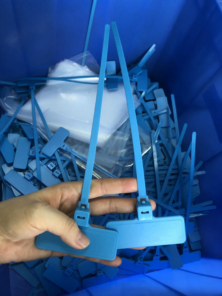 มือถือ RFID zip tie แท็ก รุ่น Z31079-1 สีน้ำเงินสองเส้นเหนือกล่องบรรจุชิ้นส่วน แสดงหัวล็อกและพื้นผิวสายรัดระหว่างการผลิต