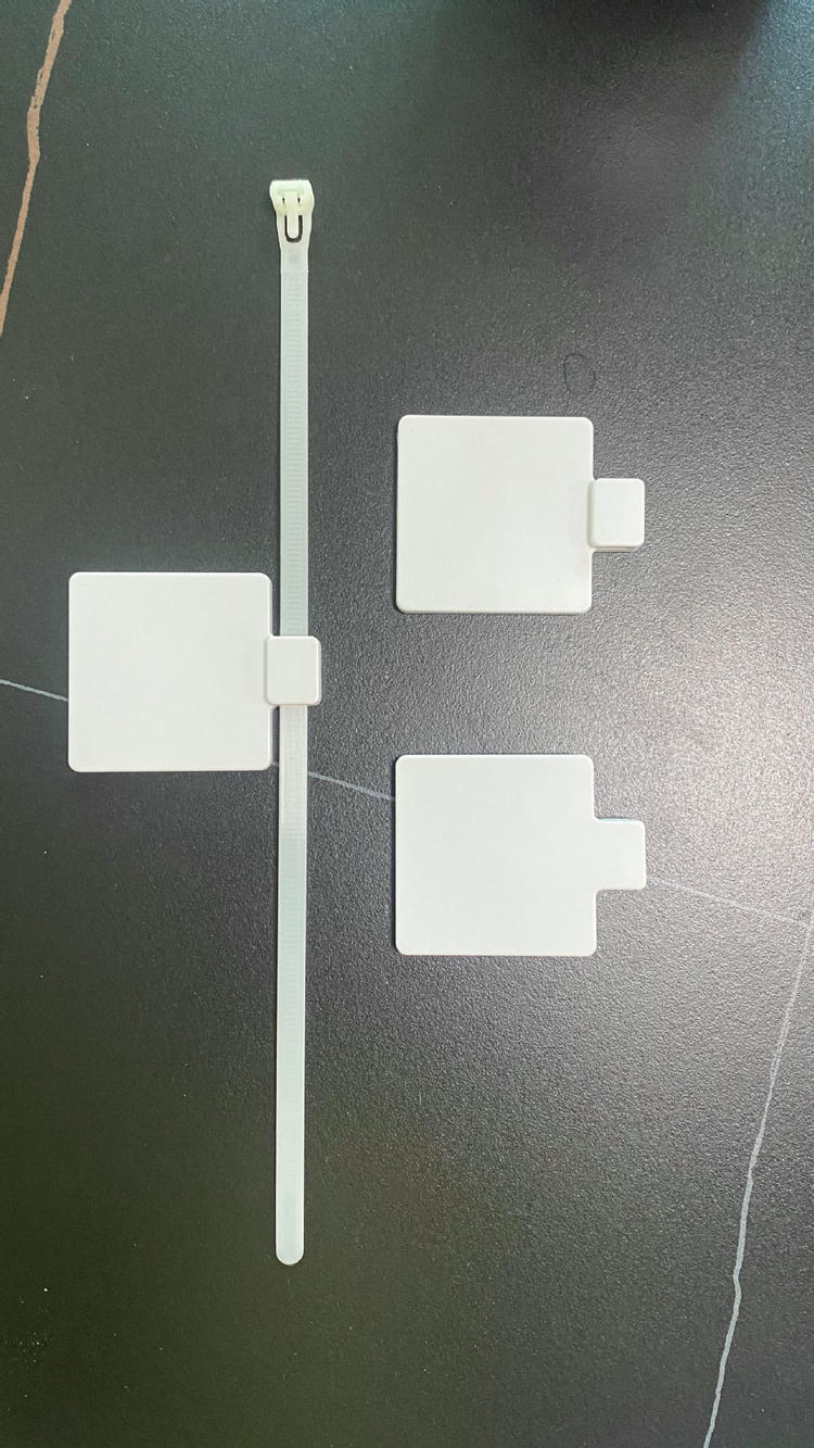 ภาพวางแบนแสดง RFID zip tie แท็ก รุ่น Z5555-1 พร้อมสายรัดไนลอนยาวข้างตัวแท็กสี่เหลี่ยมสามชิ้นที่แสดงรูปทรงหัวที่แตกต่างกัน