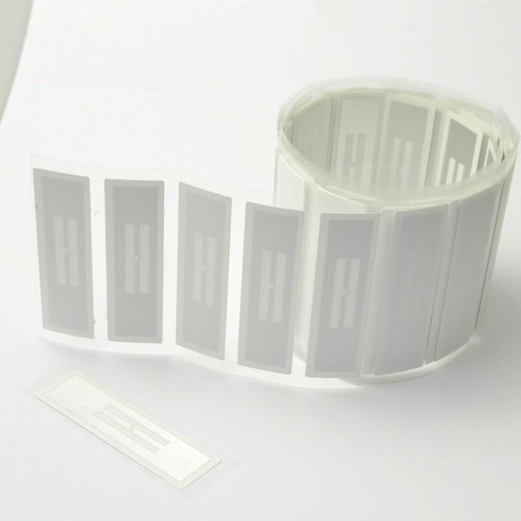ภาพถ่ายผลิตภัณฑ์ที่สะอาดแสดงฉลาก RFID ที่ต้านทานของเหลวในรูปแบบม้วน โดยมีฉลากหนึ่งแผ่นที่แยกออกมาวางอยู่ด้านหน้า