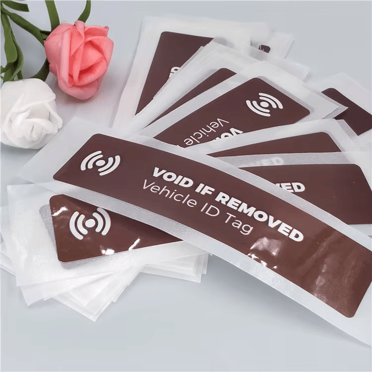 7) ภาพนี้แสดงแท็กกระจกหน้า UHF RFID สำหรับจัดการยานพาหนะ VOID IF REMOVED โดยเน้นคุณสมบัติด้านความปลอดภัยและป้องกันการแกะย้าย และตำแหน่งล็อกและคุณสมบัติป้องกันการสูญหาย โดยจัดเรียงให้เปรียบเทียบรายละเอียดได้ชัดเจน สำหรับงานยานพาหนะ ยางรถ และการจัดการกองรถ.