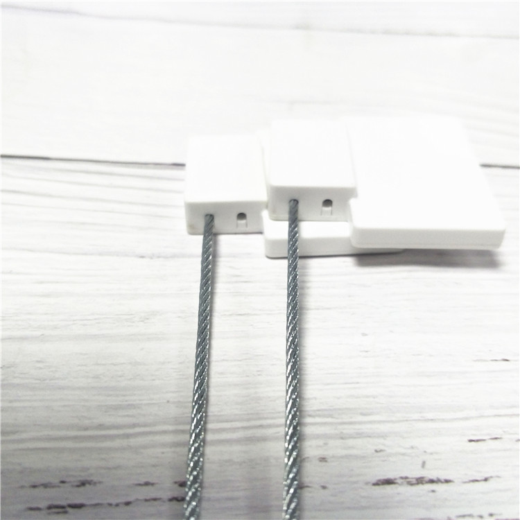 ภาพด้านข้างระยะใกล้แสดงตัวเรือนซีลนิรภัย RFID รุ่น SS4544-1 สีขาวสองชิ้นพร้อมสายเคเบิลเหล็กบนพื้นผิวลายไม้