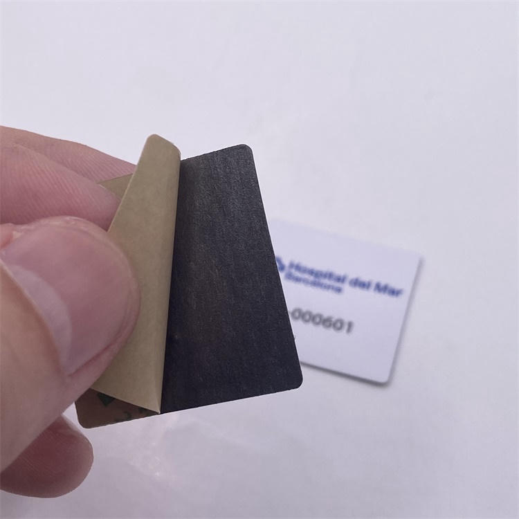 ภาพระยะใกล้ของมือที่กำลังลอกแผ่นรองหลังออกจาก RFID แท็ก ชนิด PVC สำหรับติดบนโลหะ แสดงชั้นกาวที่พร้อมยึดติดกับอุปกรณ์โลหะ