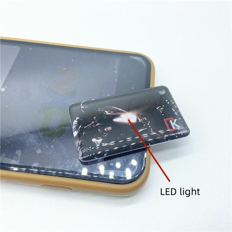 2) ภาพนี้แสดงนามบัตร NFC LED เคลือบอีพ็อกซีพร้อมไฟตอบรับไร้แบตเตอรี่ โดยเน้นอีพ็อกซี และไฟแสดงสถานะ LED.