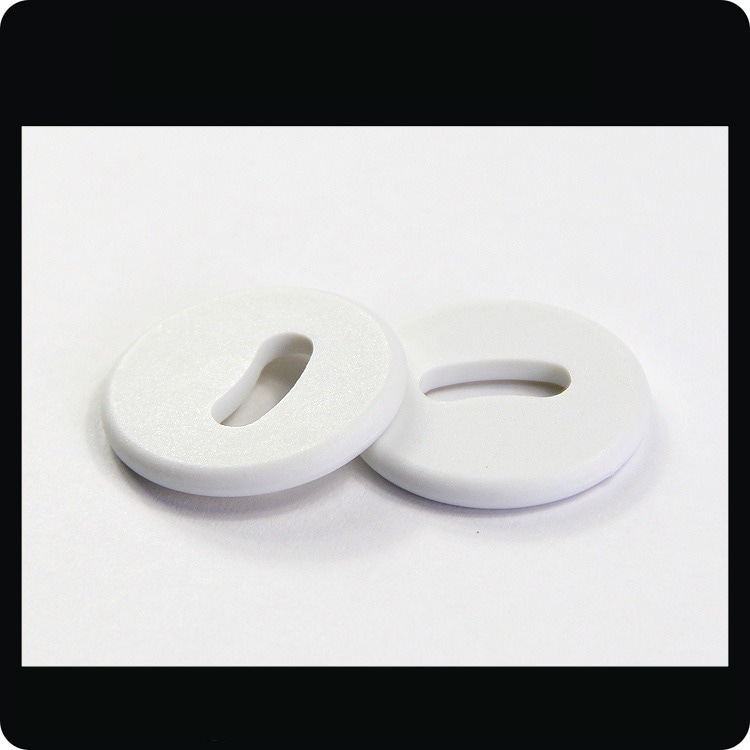 แท็กซักผ้า RFID PPS สีขาวสองชิ้นรุ่น PPSD26-1 พร้อมรูจันทร์เสี้ยวถูกถ่ายภาพเพื่อแสดงรูปลักษณ์ที่สะอาดสำหรับการติดตามผ้าลินิน