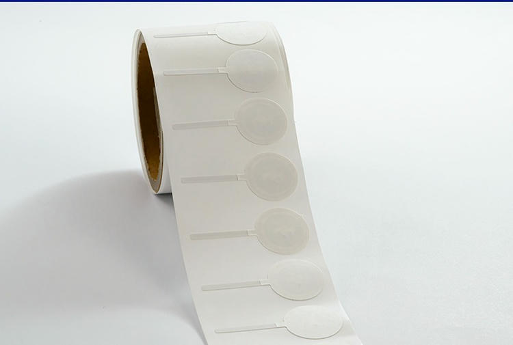 ภาพระยะใกล้ของแถบฉลาก RFID ป้องกันการแกะแบบม้วนแสดงฉลากความปลอดภัยฝาขวดกลมหลายดวงบนกระดาษรอง