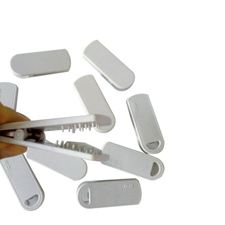 ภาพนี้แสดงมือกำลังเปิด SV-014 RFID clip แท็ก ขณะที่มีตัวแท็กหลายอันกระจัดกระจายอยู่รอบผลิตภัณฑ์