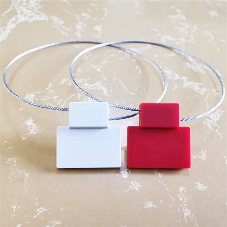 ซีลนิรภัย RFID รุ่น SS4544-1 สีขาวและสีแดงวางเคียงข้างกันพร้อมห่วงสายเคเบิลเหล็กบนพื้นผิวสไตล์หินอ่อน