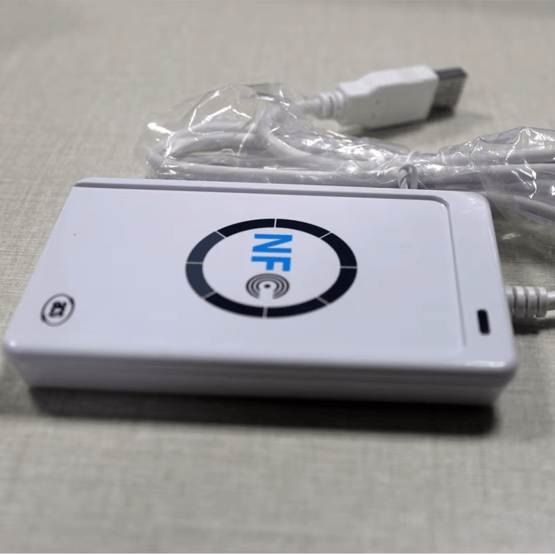 ภาพนี้แสดงความหนาของเครื่องอ่าน ACR122U แบบโปรไฟล์เตี้ย โดยมีสาย USB และหัวต่อปรากฏอยู่ด้านหลังเพื่อใช้อ้างอิงขนาด
