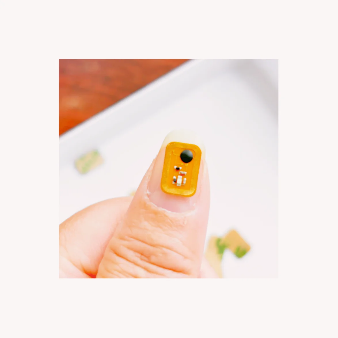 แท็ก NFC LED FLED1006-1 หนึ่งชิ้นวางอยู่บนนิ้วหัวแม่มือเพื่อแสดงให้เห็นขนาดที่เล็กมากและการออกแบบ FPC สี่เหลี่ยม